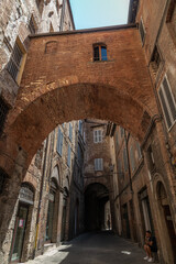 Fototapeta na wymiar Narrow Street in Historic Center of Siena, Tuscany, Italy. Old brick and stucco houses, arches and cobblestone pavement
