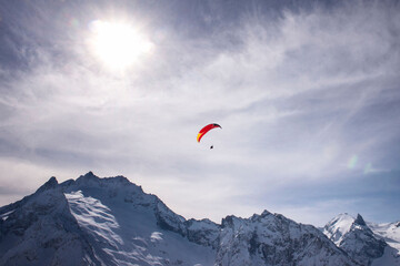 Bright red paraglider on a winter cloudy day flies over the snow-capped mountains of the Caucasus Range