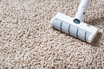 A cordless vacuum cleaner cleans the carpet in the living room with the bottom of the legs With a clean stripe