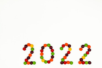 The inscription of the new year 2022 with multi-colored candy pins on a white background. The inscription is located at the bottom right, Top view. 