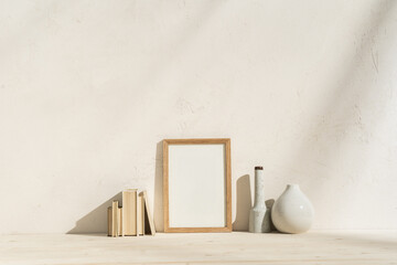 Portrait wooden frame mockup on a table. Modern ceramic vase and books with sun reflections on the...