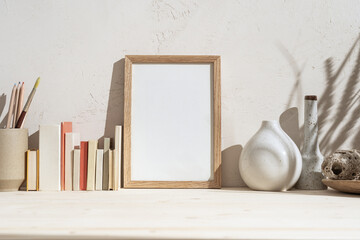 Portrait wooden frame mockup on a stack of books. Decorative stones, drawing pencils and natural...