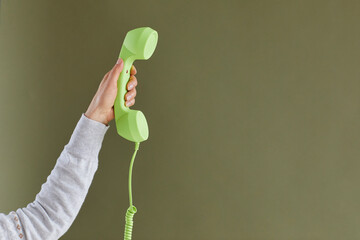 Human hand holding receiver of retro phone. Cropped shot of young lady raising up bright green...