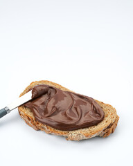 Slice of whole wheat toast with healthy chocolate hazelnut spread, knife on white background, space for text.