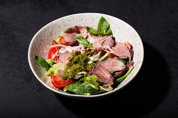 salad with roast beef and oyster mushrooms, herbs, cherry, basil and pesto sauce, black background, hard light