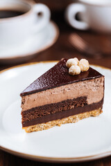 Chocolate hazelnut cake with five layers of biscuit and cream with chocolate glazing on top and whole nuts from Piemont. Served and decorated with coffee in background