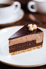 Chocolate hazelnut cake with five layers of biscuit and cream with chocolate glazing on top and whole nuts from Piemont. Served and decorated with coffee in background
