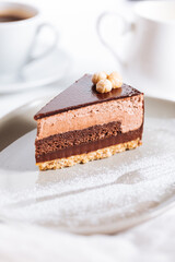 Chocolate hazelnut cake with five layers of biscuit and cream with chocolate glazing on top and whole nuts from Piemont. Served and decorated with coffee in background