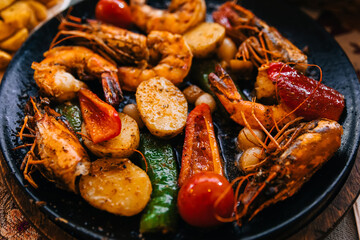 Shrimps and crayfish, grilling, with vegetables and potatoes on a black plate on the table.