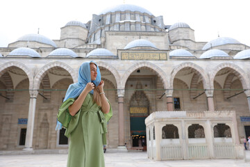 a young woman in a headscarf and dress walks through the territory of the Blue Mosque in Istanbul.