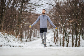 Fit sportsman skipping the rope in nature at snowy winter day. Winter fitness, cardio exercises