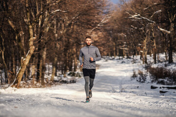 Fototapeta na wymiar Sportsman running on snowy path in woods at winter. Winter sport, healthy habits, outdoor fitness