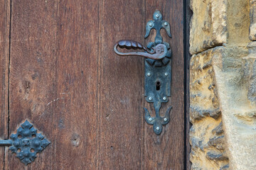 Fragment of an old dark wooden door. There are metal fittings and a black door handle. Part of the stone wall is visible. Background. Texture.