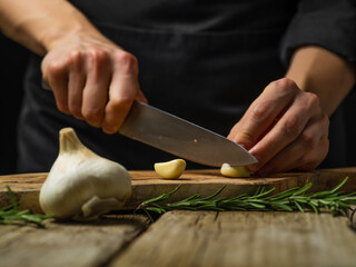 Close-up. The chef cuts the garlic on a cutting board. a sprig of rosemary lies nearby. Rough...