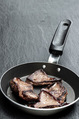 Fried livers with herbs in a frying pan on black stone background