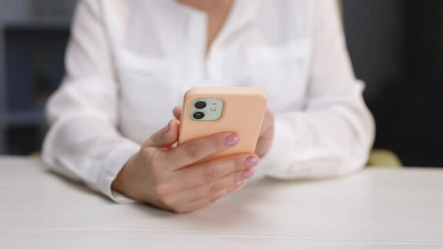 Woman holds mobile phone and swipes photos or pictures left indoors of cozy home. Close up of woman using smartphone pressing finger, reading social media internet, typing text or shopping online