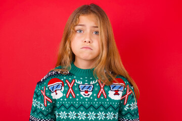 little kid girl wearing knitted sweater christmas over red background crying desperate and depressed with tears on his eyes suffering pain and depression. Sad facial expression and emotion concept.