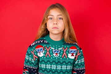 Joyful little kid girl wearing knitted sweater christmas over red background looking to the camera,...