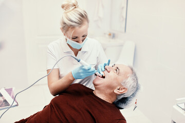 Fototapeta premium Woman doctor dentist works with an elderly man in a dental chair treats teeth and shows x-rays