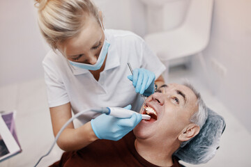 Obraz na płótnie Canvas Woman doctor dentist works with an elderly man in a dental chair treats teeth and shows x-rays