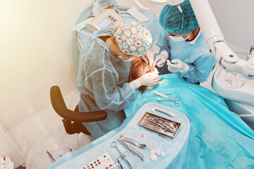 
2 women dentists perform dental implantation operations on a patient in a dental clinic in special clothes