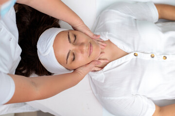 Fototapeta na wymiar High angle view of a young Caucasian woman receiving face and neck massage during beauty treatment in cosmetic salon