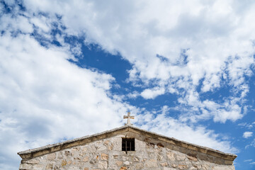 Fototapeta na wymiar The top of the church with a cross against a bright blue sky. Part of the temple is made of white stone. Minimalist frame of architecture. Pure colours
