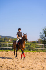 Young caucasian girl riding on a horse with a brown horse, dressed in black rider with safety hat