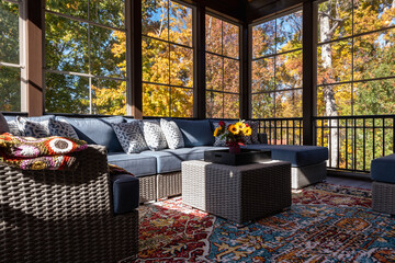  Cozy screened porch with contemporary furniture and flower bouquet in a vase, autumn leaves and woods in the background.