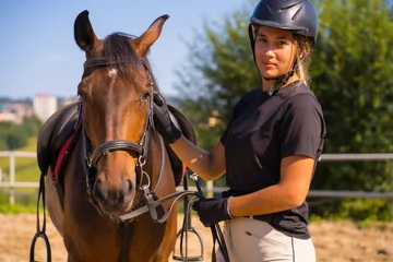 Foto op Canvas Posing of a Caucasian blonde girl on a horse caressing and pampering a brown horse, dressed in black rider with safety cap © unai
