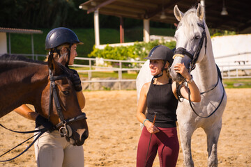 Two young Caucasian girl riders with their white and brown horses on a horse riding, dressed in black with safety caps