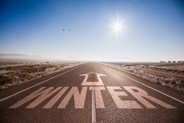 Carretera desierta en invierno con letras en el asfalto y una flecha que simboliza la llegada del invierno