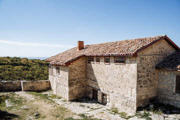 Fototapeta na wymiar Old house with a tiled roof in the mountain plains. Large stone house. Bright blue sky, clear mountain air and green forests. Rest in the mountains