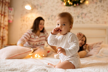 beautiful Christmas family photo. A child in white clothes sits on the bed at home and looks at the...