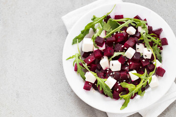 Beetroot, cottage cheese and arugula salad with white and black sesame seeds on a plate on a light gray background top view copy space