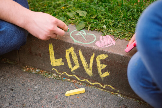 The word love written in chalk on curb and couple hands drawing with chalk