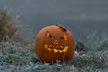 Close-up view of orange Halloween pumpkin with carved Jack O'Lantern face lying on frozen grass...