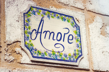 Word amore drawn with blue paint on wooden plaque decorated with flowers