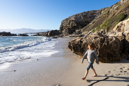 A young boy alone on a small stretch of sand under the cliffs by the ocean.