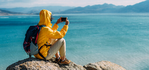 A girl traveler on the background of the sea. The concept of adventure, travel and hiking. A traveler with a phone on the background of the sea, panorama. A man in tourist clothes by the sea