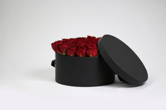 Black round gift flower packaging box with red roses inside and opened lid. Stylish flower arrangement.