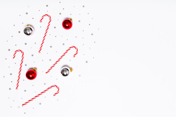 Christmas flat lay composition. Christmas candy canes, red and silver balls, silver glitter confetti stars on white background. Flat design, top view, copy space.