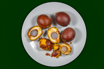 Buriti fruit (Mauritia flexuosa) in fine botanical and morphological details of the texture of the skin and fruits cut in half showing the interior of the fruit. Top view in green background