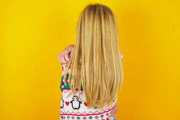 caucasian little kid girl wearing knitted sweater christmas over yellow background hugging herself happy and positive from backwards. Self love and self care