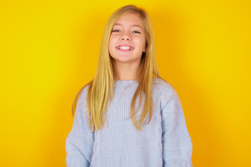 caucasian kid girl wearing blue knitted sweater over yellow background with a happy and cool smile on face. Lucky person.