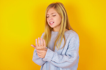 caucasian kid girl wearing blue knitted sweater over yellow background Suffering pain on hands and...