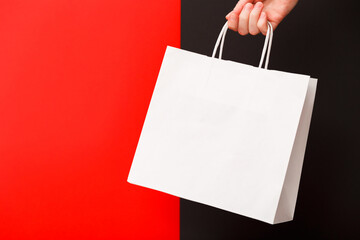 Female hand holding white blank shopping bag isolated on red and black background. Black friday sale, discount, recycling, shopping and ecology concept.