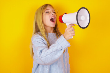 caucasian kid girl wearing blue knitted sweater over yellow background  Through Megaphone with...