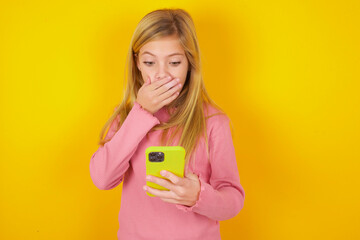 caucasian little kid girl wearing long sleeve shirt over yellow background being deeply surprised,...