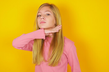 caucasian little kid girl wearing long sleeve shirt over yellow background cutting throat with hand...